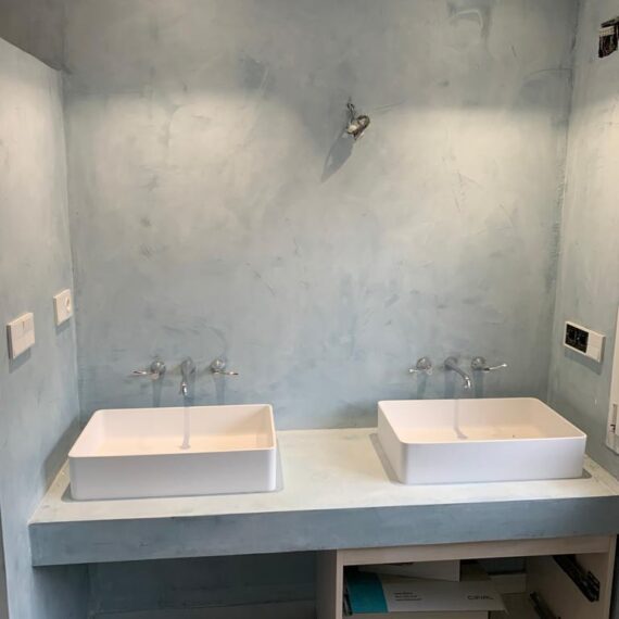 Dúo de lavamanos blancos con acabados grises en pared de reforma en casa de Toledo